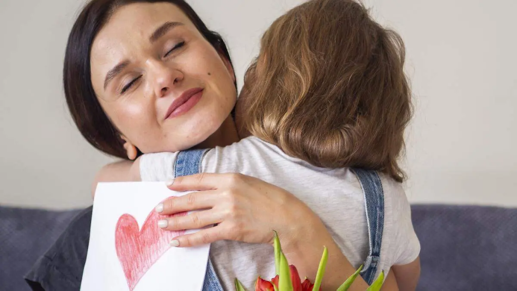 Two People Share a Warm Hug; One Holds a Card with a Red Heart and a Bouquet Nearby. - Capitanes Regios