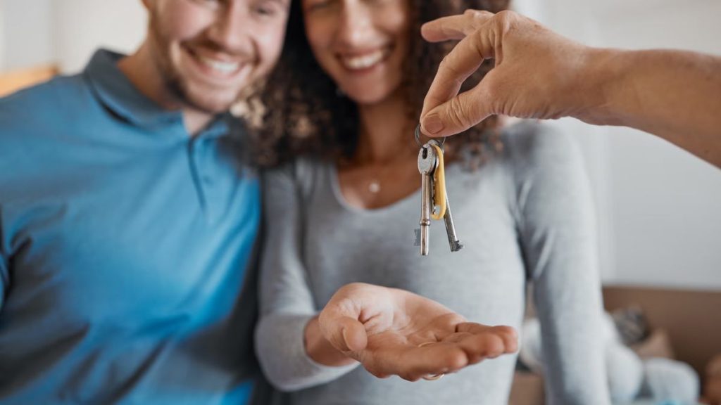 a Person Hands a Set of Keys to a Smiling Couple, Suggesting a Home Handover or New Key One Purchasing a House. - Capitanes Regios