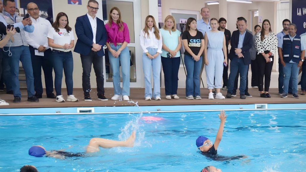 a Row of Adults Standing on a Pool Deck Watching Two Swimmers in the Pool Wearing Caps and Goggles. - Capitanes Regios