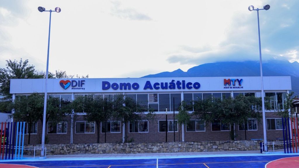 Exterior View of the Domo Acuático Aquatic Center with Dif Monterrey Logo and Mty Sign, Trees in Front, and Mountains in the Background. - Capitanes Regios