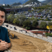 Smiling Man in a Teal Polo Stands at the Edge of a Construction Site Overlooking a Costco Store and a Busy Parking Lot with Hills in the Background. - Capitanes Regios