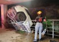 White Suv Crumpled Against a Railing, Tilted over a Drop in a Dimly Lit Underpass; Emergency Responder in Helmet Observes from the Railing Edge. - Capitanes Regios