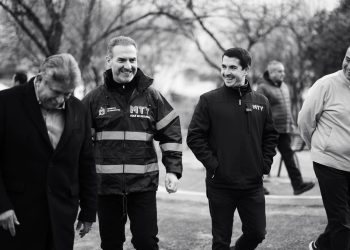 Four Men Walking Outdoors, Smiling and Talking; One Wears a High‑visibility Jacket with Mty Branding (black and White).趙 - Capitanes Regios