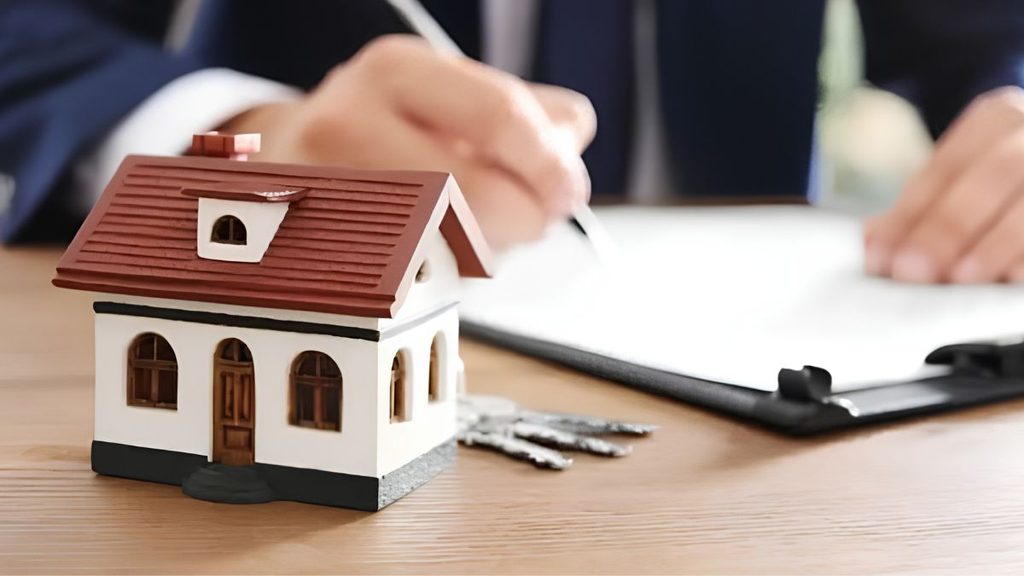 Person Signing Real Estate Documents at a Desk, with a Miniature House Model and Keys Nearby, Symbolizing a Property Closing - Capitanes Regios