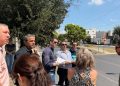 Group of People Standing on a Sunny Street Corner, Holding Papers and Talking, with Trees and a Stop Sign in the Background. - Capitanes Regios