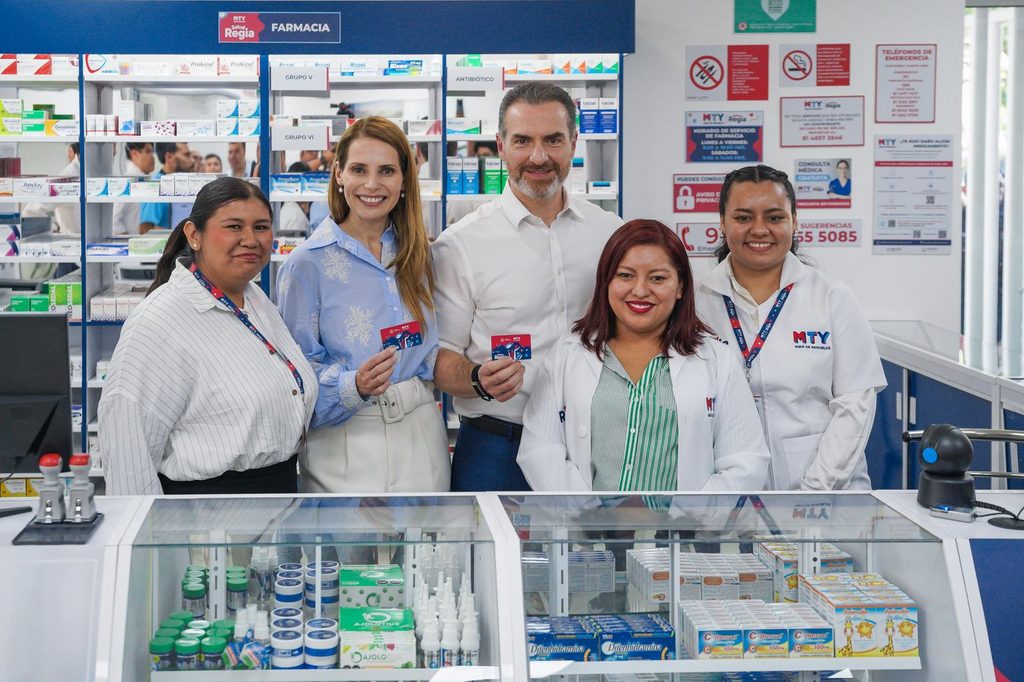 Five People, Pharmacists, Smiling at the Counter with Medicine Shelves Behind Them in a Pharmacy Setting. - Capitanes Regios