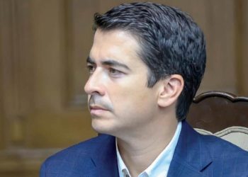 Man in a Blue Suit Seated at a Table with a Microphone in Front, Looking to the Left in a Formal Meeting Room - Capitanes Regios
