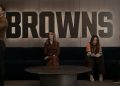 Four People Sit on a Dark Sofa in a Modern Room, with a Large Browns Sign on the Wall Behind Them; a Man Stands at Left While Two Women and Another Man Sit. - Capitanes Regios