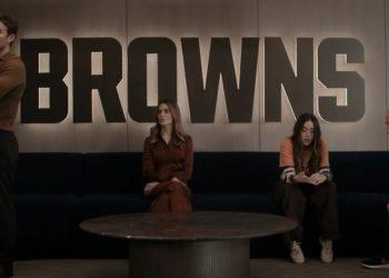 Four People Sit on a Dark Sofa in a Modern Room, with a Large Browns Sign on the Wall Behind Them; a Man Stands at Left While Two Women and Another Man Sit. - Capitanes Regios