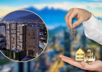 Two Hands Hold a Small Model House and Keys in Front of a Blurred City Skyline, Suggesting Property Ownership or Real Estate Investment. - Capitanes Regios